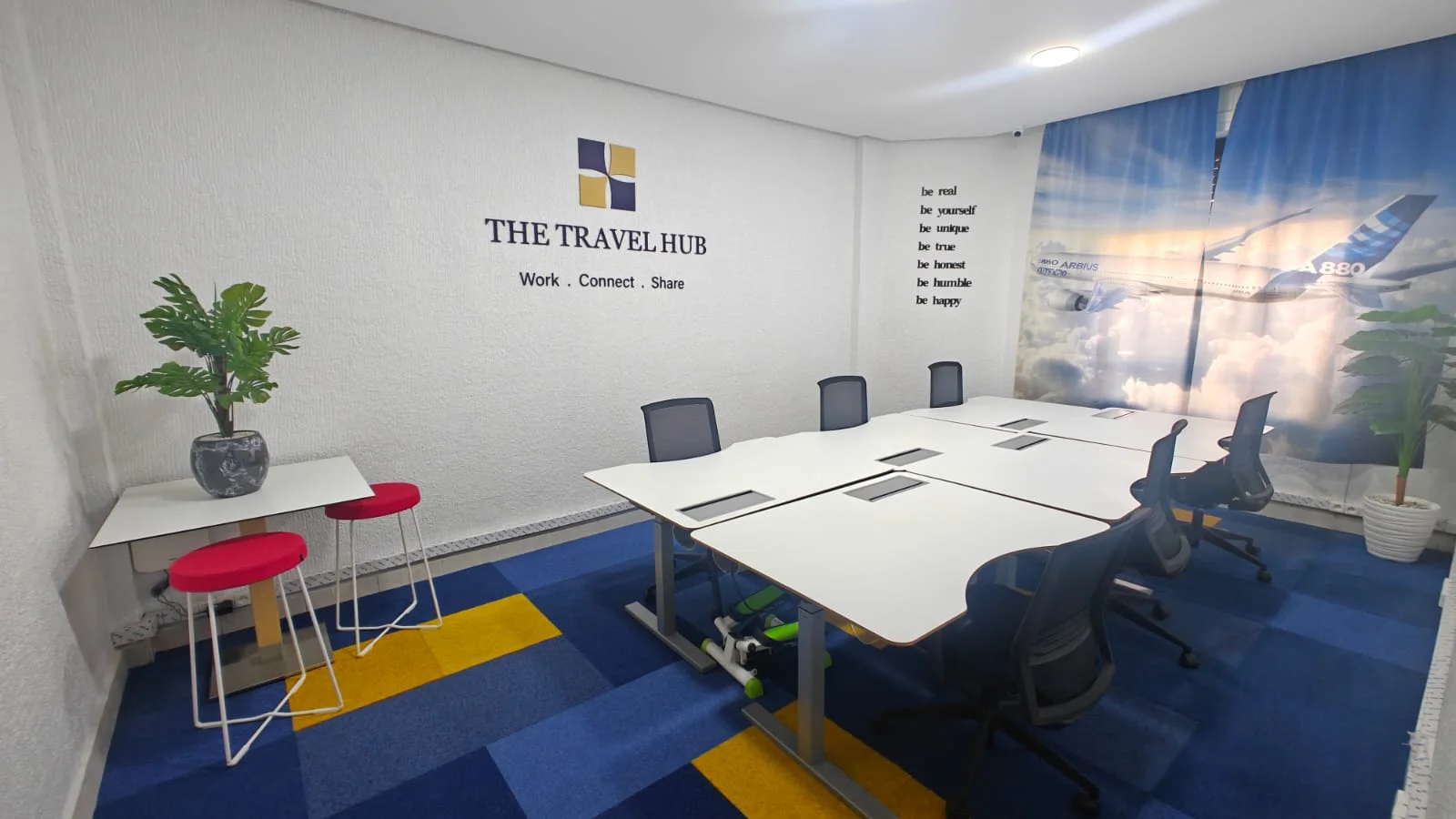 The actual Travel Hub coworking room in Rabat, with white sit-stand desks, office chairs and travel-inspired décor